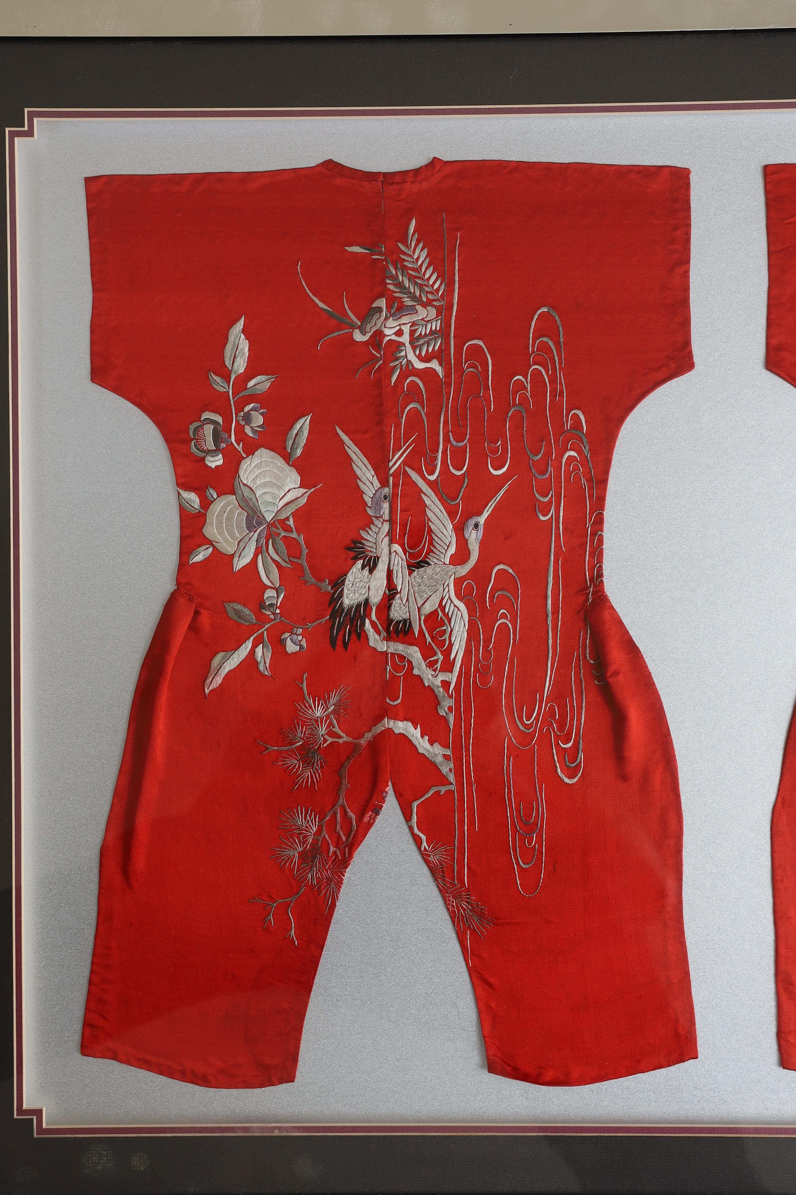 Three early 20th century Chinese framed embroideries: two purple baby’s bibs embroidered with multi-coloured silk threads, and another red silk child’s “romper suit”, embroidered with white and pastel embroidery, mounted